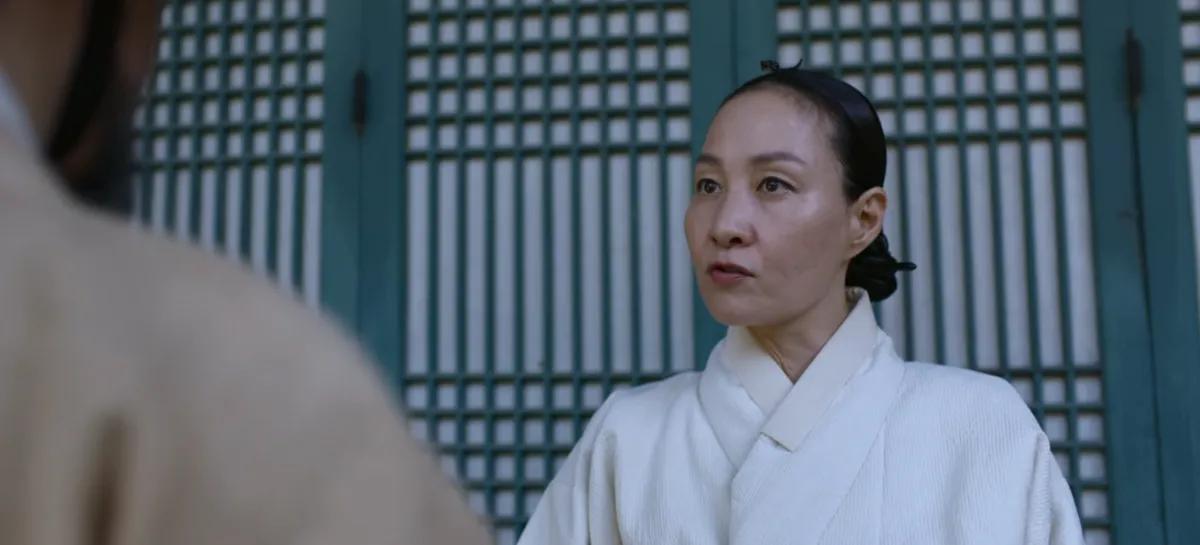 Una mujer vistiendo ropas tradicionales blancas frente a una estructura tradicional coreana, escena de 'Kingdom' de Netflix.