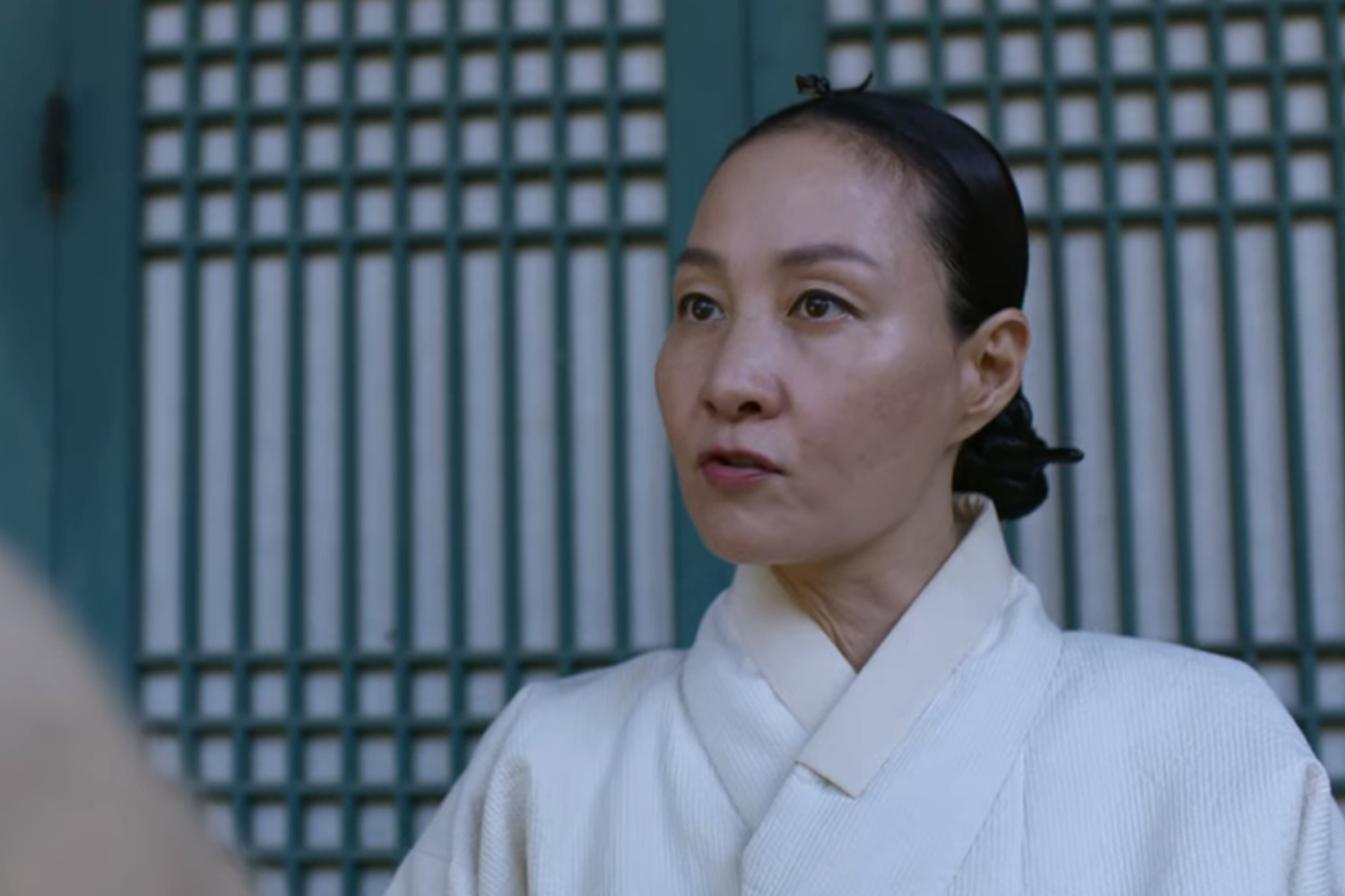 《屍戰朝鮮》中中殿媽媽穿著白色宮中服飾,站在宮殿前。