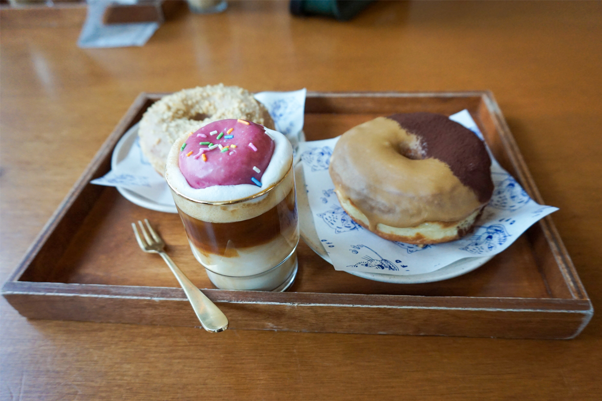 一组甜品展示盘,上面有不同口味的甜甜圈,包括草莓、花生酱和提拉米苏甜甜圈,以及一杯拿铁。