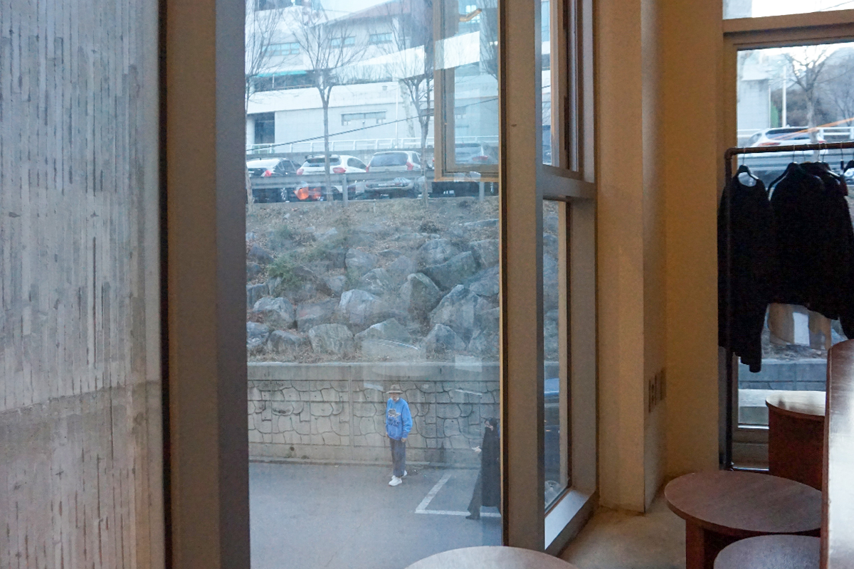 通过咖啡馆的窗户看向外面的景色,窗外是一个停满汽车的停车场,背景有一座建筑物。