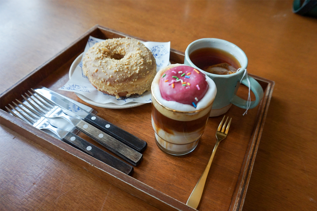 一个托盘内放置的甜甜圈和饮品,包括一个花生酱甜甜圈和一杯上面放有小甜甜圈的拿铁。