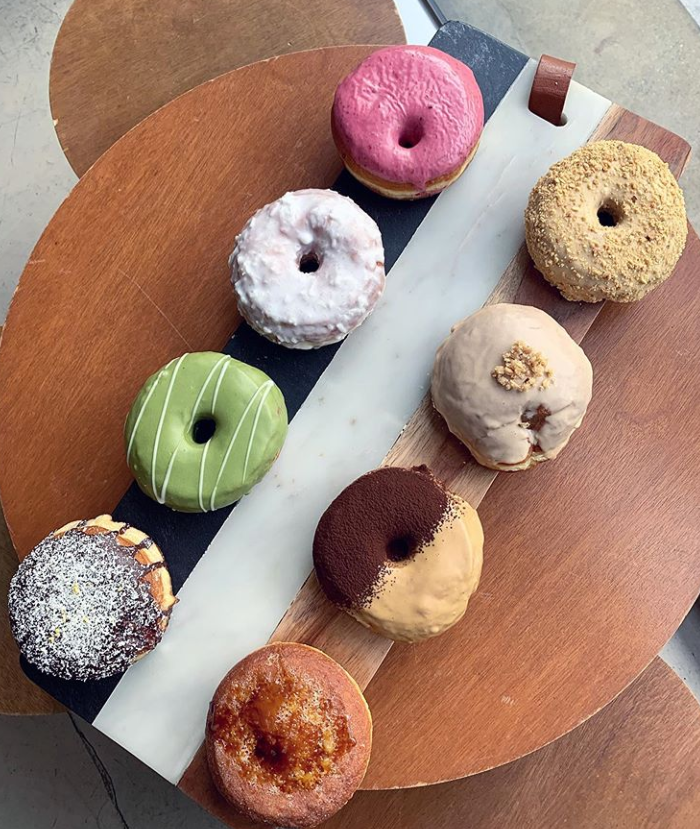 Old Ferry Donut咖啡馆提供的多种口味甜甜圈,展示在一个木制的托盘上,包括有抹茶、草莓和花生酱等口味。