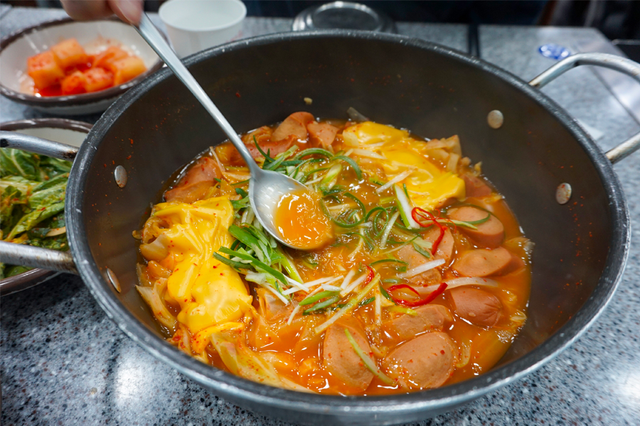 顾客在大海食堂享用部队锅，使用汤勺品尝美味的韩式汤底。