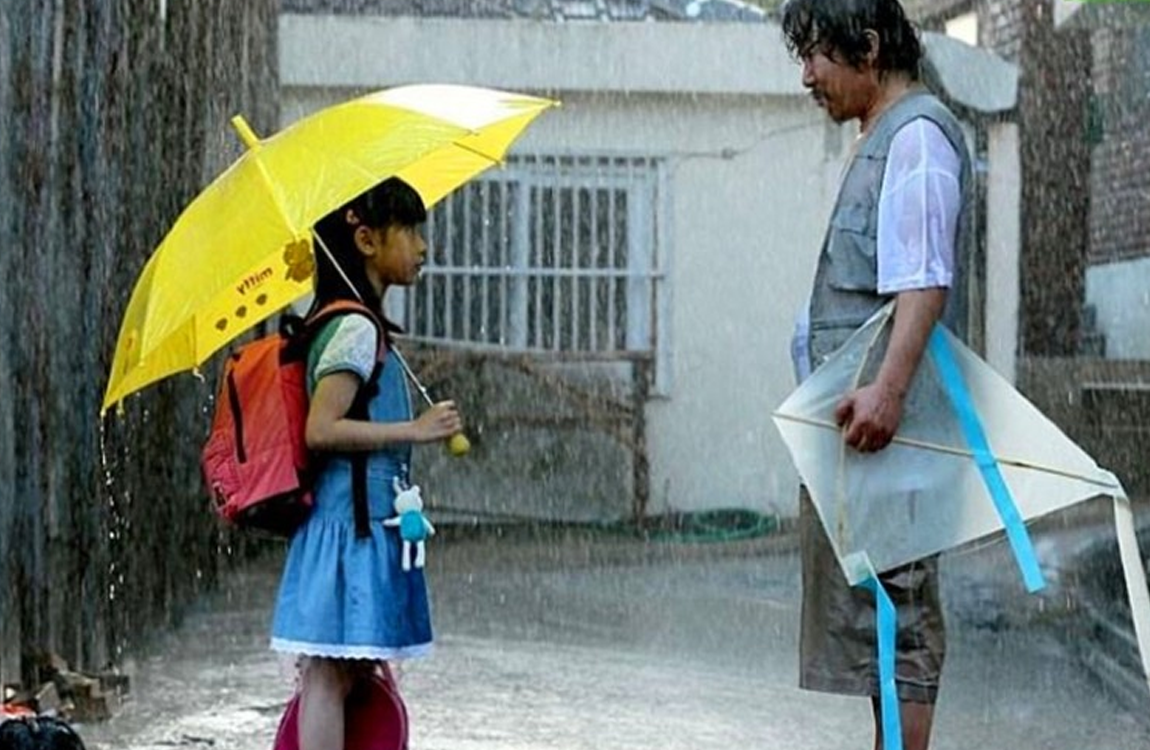 電影《希望：為愛而生》中，小女孩和成年男子站在雨中，女孩打著黃色雨傘，反映了故事中一個關鍵場景。