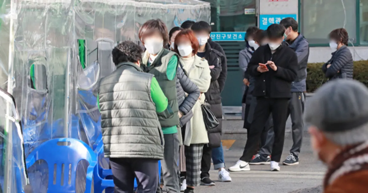 數名韓國人在戶外排隊，背景顯示街道上的透明塑料帳篷，反映當地某個活動或等待的日常景象。