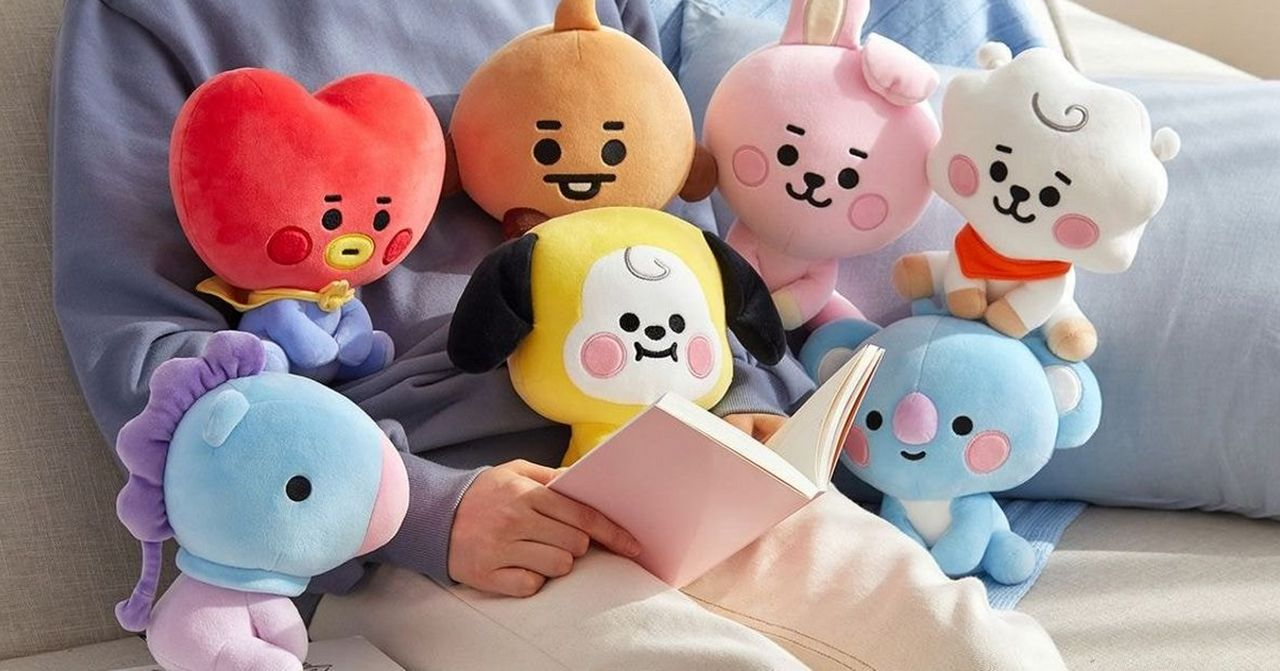 ตุ๊กตา BT21 เบบี้หลากหลายสีสัน เอนกายอยู่บนโซฟา พร้อมกับหนังสือเล่มหนึ่งในมือของเจ้าของ