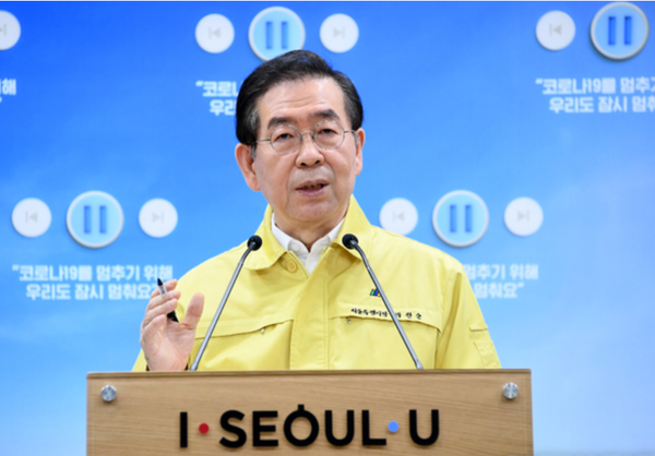 首爾市政府官員正在解釋災難生活費的細節，背景是首爾的市政標誌。《자료：서울시정부》