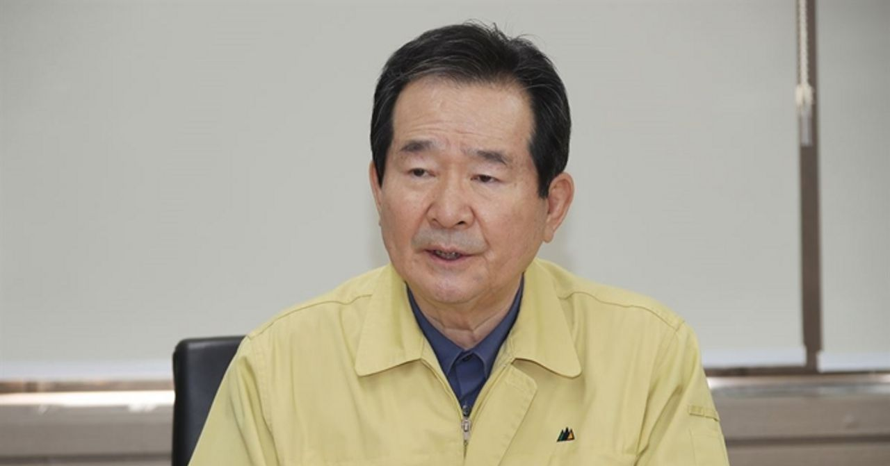 韩国官员在会议中穿着黄色工作服，背景为公司办公室的墙壁。