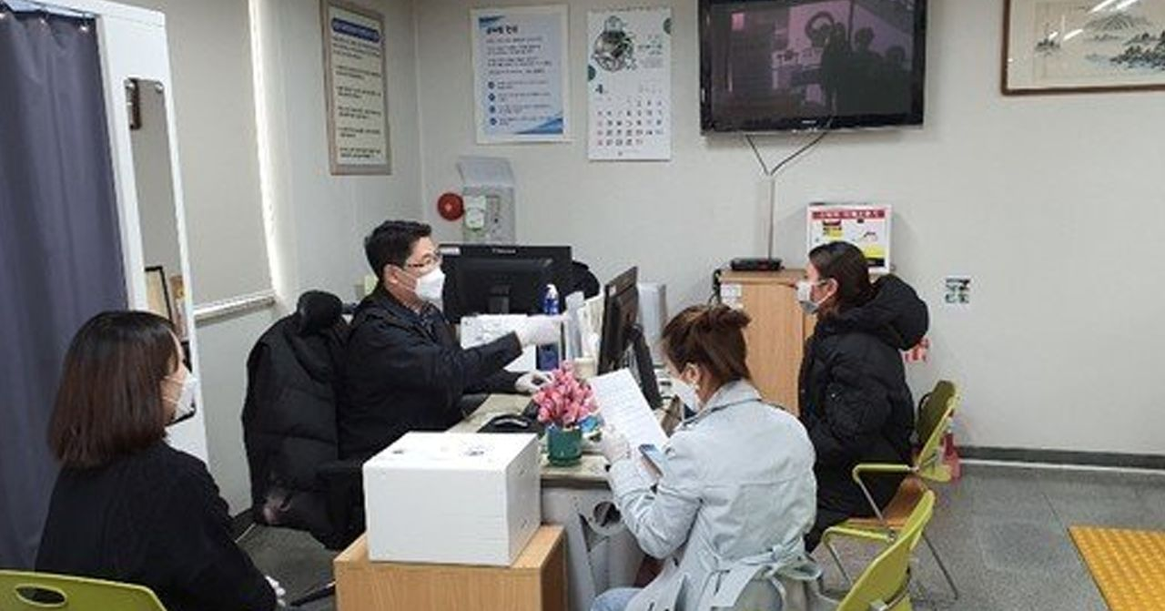 韩国办公室场景，两人佩戴口罩坐在办公桌前交流，以应对新冠疫情。