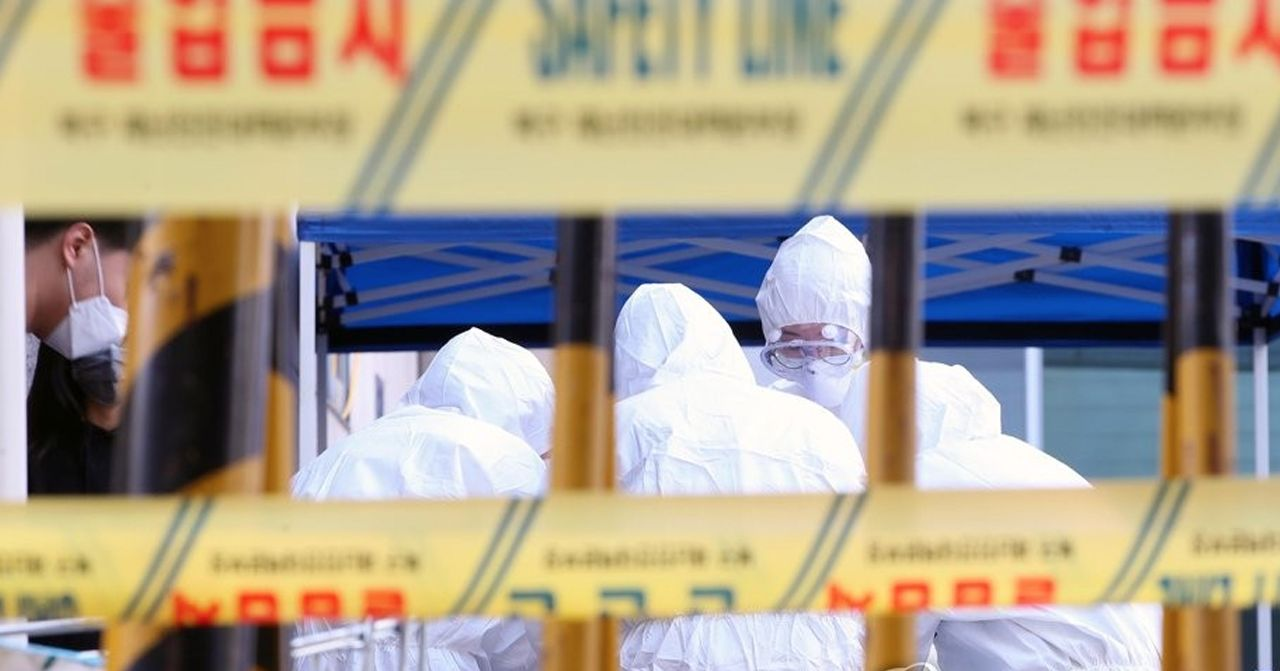 配戴高防護裝備的工作人員在COVID-19核酸檢測站點進行工作，周圍有黃色的安全防護線