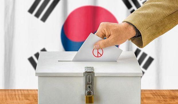 手持選票放入投票箱的示意圖，背景是韓國國旗。