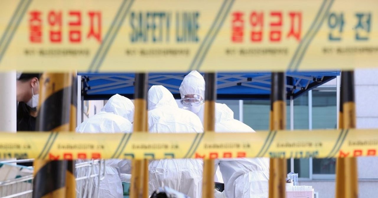 穿戴防護裝備的工作人員在防疫現場協調工作，背景有黃色安全警戒標誌，象徵著抗疫努力和嚴謹。」