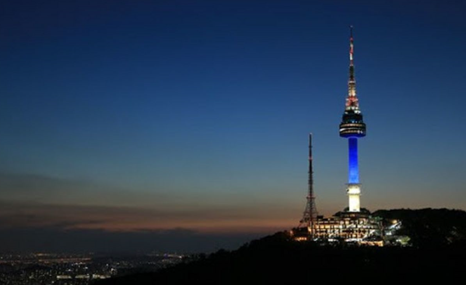 夜空にライトアップされたソウルのタワーが見え、青い光が特に強調されています。