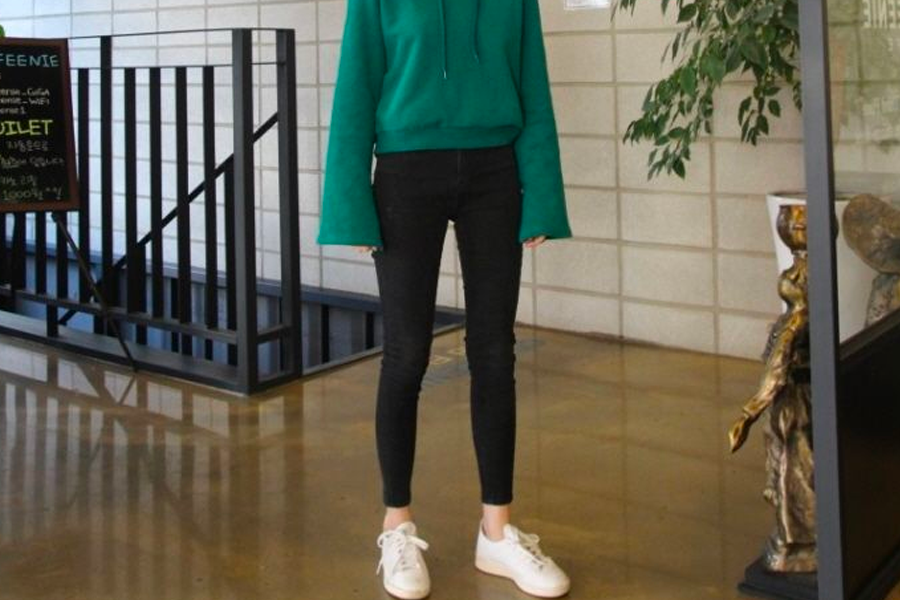 Casual style in South Korea showcasing comfortable attire for transitional weather, featuring a green hoodie and black jeans paired with white sneakers, typical of spring or fall.