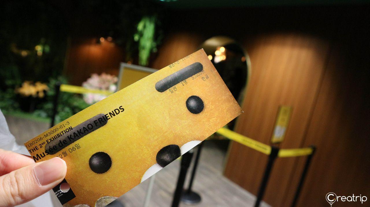 Kakao Friends themed entry ticket being held up near the ticket counter inside the museum.