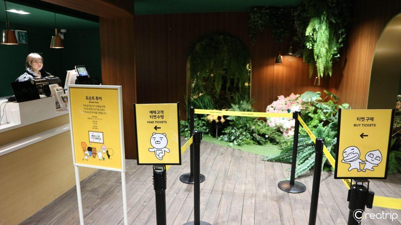Kakao Friends ticket counter area with plants and signs for ticket purchases.