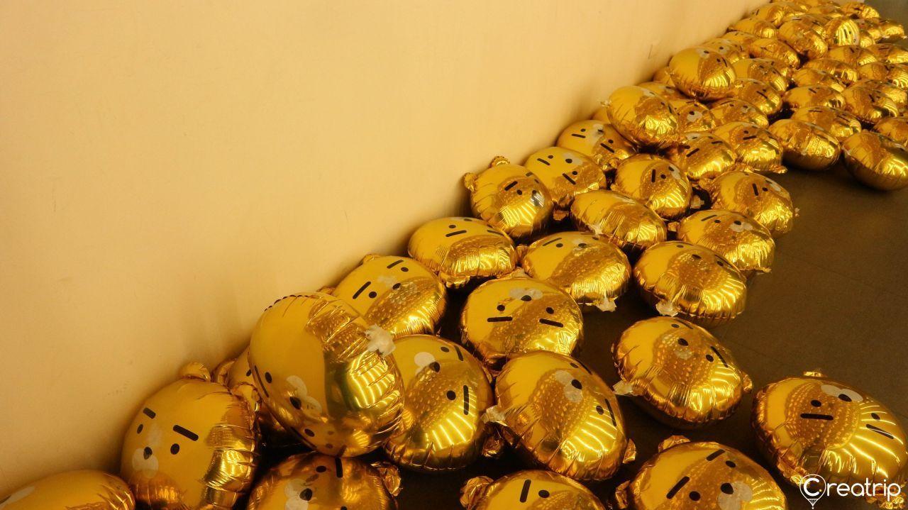 Pile of golden Ryan-themed balloons scattered on the floor of an exhibition room.