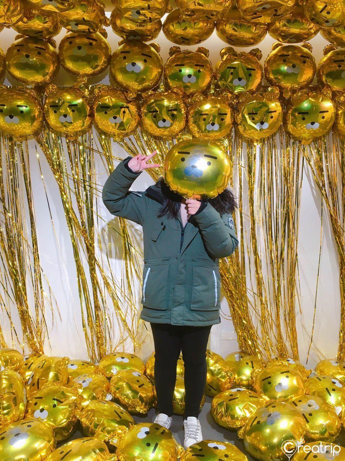 Museum guest holding a golden balloon amidst colorful Kakao Friends themed decorations.
