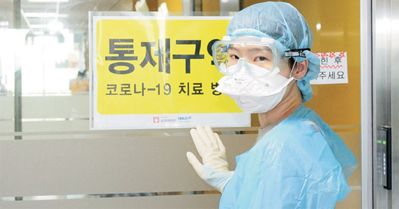 穿著防護裝的醫護人員站在寫著韓文標識的門前，戴著口罩和手套。