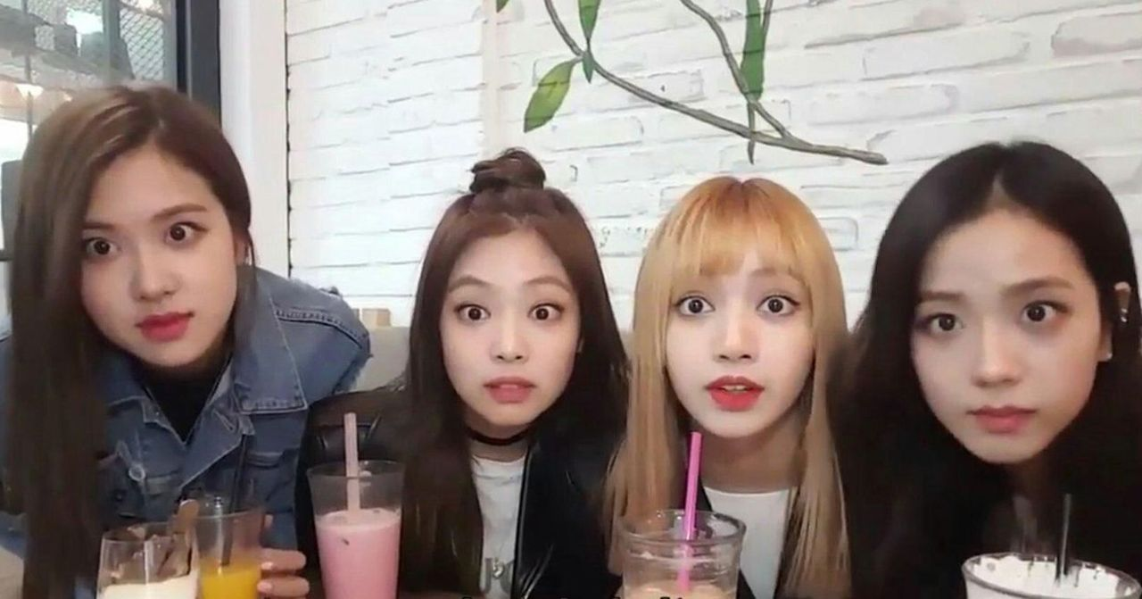 一群女性在咖啡店內，桌上擺放有多種顏色的飲料，木製桌子和白色磚牆背景，提供舒適的氛圍。