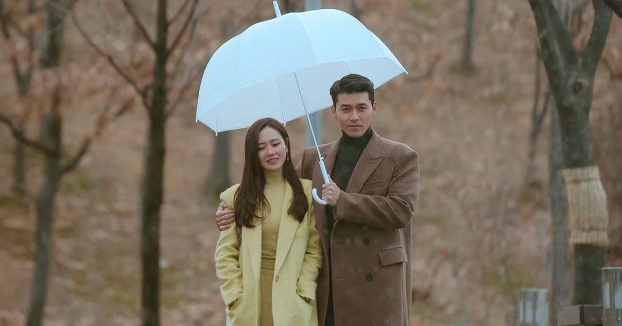 一對情侶在下雨天共用一把傘，站在樹林裡