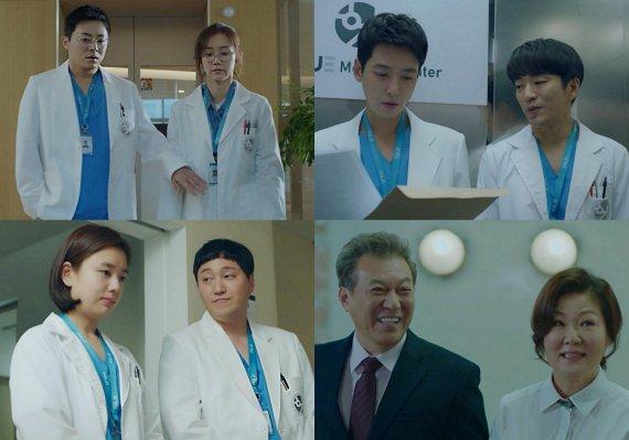 賢い医師生活のシーンから、病院の廊下またはオフィスの一部を背景に、白衣を着た2人の医師の様子。医師たちは名札をつけ、青いストラップを首にかけている。