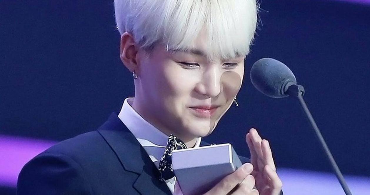 SUGA của BTS cầm một giải thưởng trong bộ vest trình diễn tại một sự kiện âm nhạc