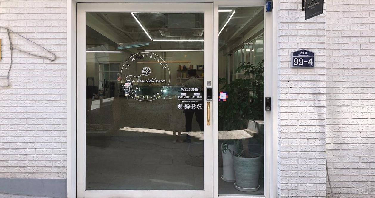 Cửa kính của quán cafe Le Montblanc với logo độc đáo tại Itaewon, Seoul. Không gian bên trong nổi bật bởi sự ấm cúng và phong cách trang trí nghệ thuật.