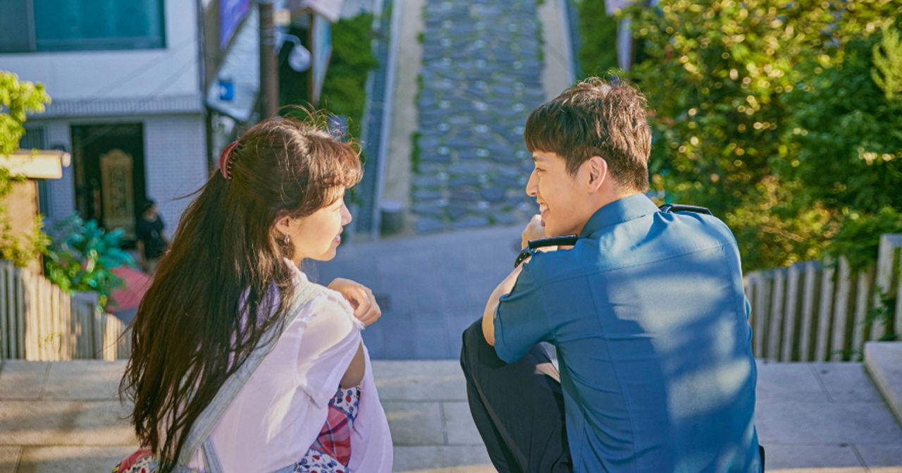 Szene aus dem koreanischen Drama 'Wenn die Kamelie blüht'. Ein Mann und eine Frau sitzen auf einer Treppe in einem Wohngebiet.