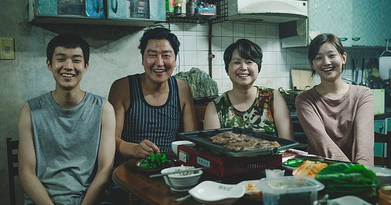 Szene aus dem koreanischen Film 'Parasite'. Mehrere Personen sitzen an einem Tisch in einem bescheidenen Raum.