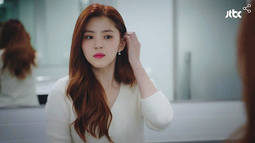 Szene aus dem koreanischen Drama 'Eine Welt der verheirateten Paare'. Eine Frau mit langen roten Haaren schaut in einen Spiegel.