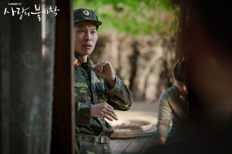 Szene aus der koreanischen Serie 'Crash Landing on You'. Eine Person in Uniform und Militäroutfit steht in einem Dorf.