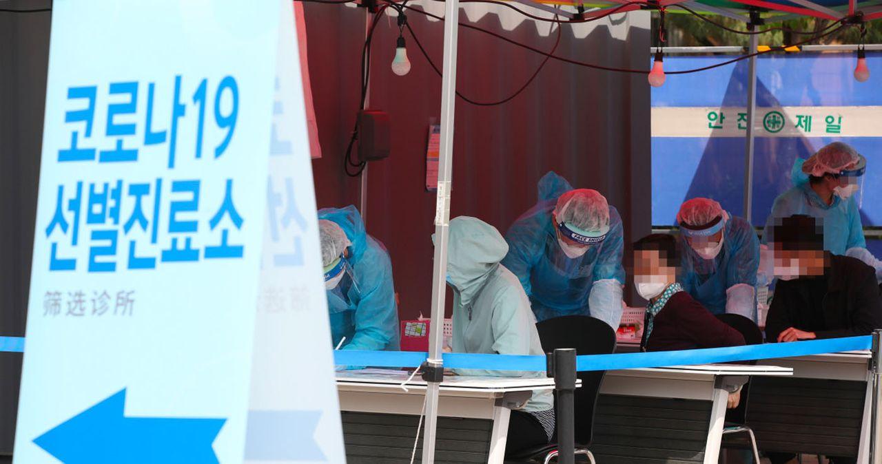 ป้ายตรวจคัดกรองโรค COVID-19 และเจ้าหน้าที่สวมชุดป้องกันกำลังทำงานที่ศูนย์ตรวจคัดกรองในเกาหลีใต้ช่วงการระบาดของโรคไวรัสโคโรนา