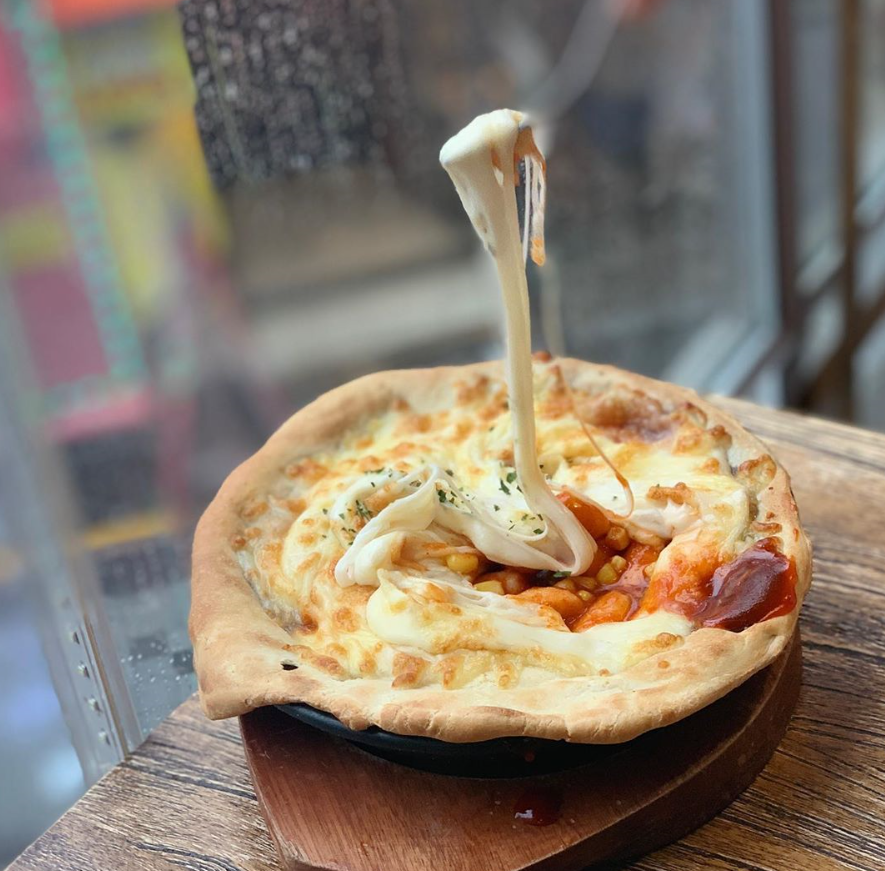 韓国風ピザのトッピングにたっぷりのチーズが伸びている画像