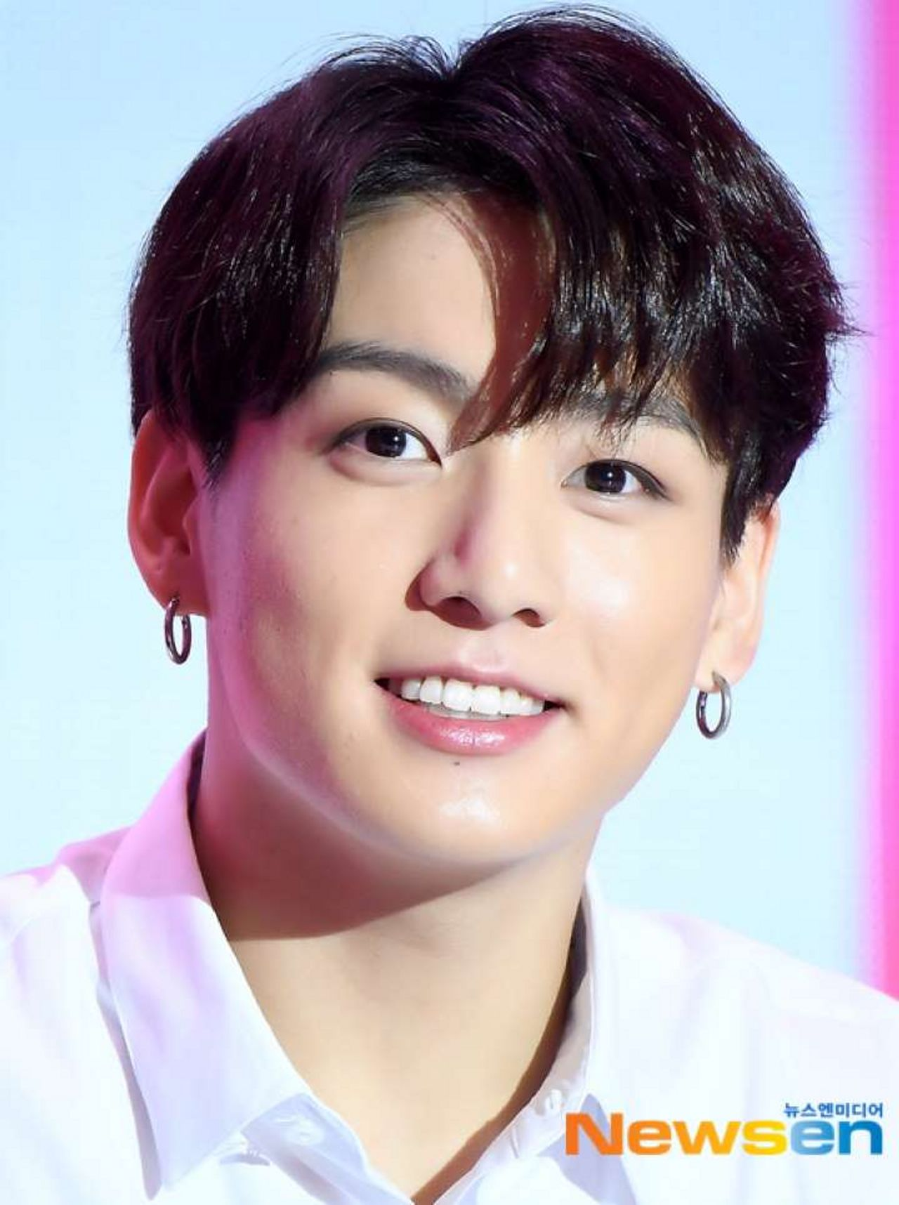 韓國著名男子偶像團體中成員的特寫照片，背景是柔和的粉色燈光。