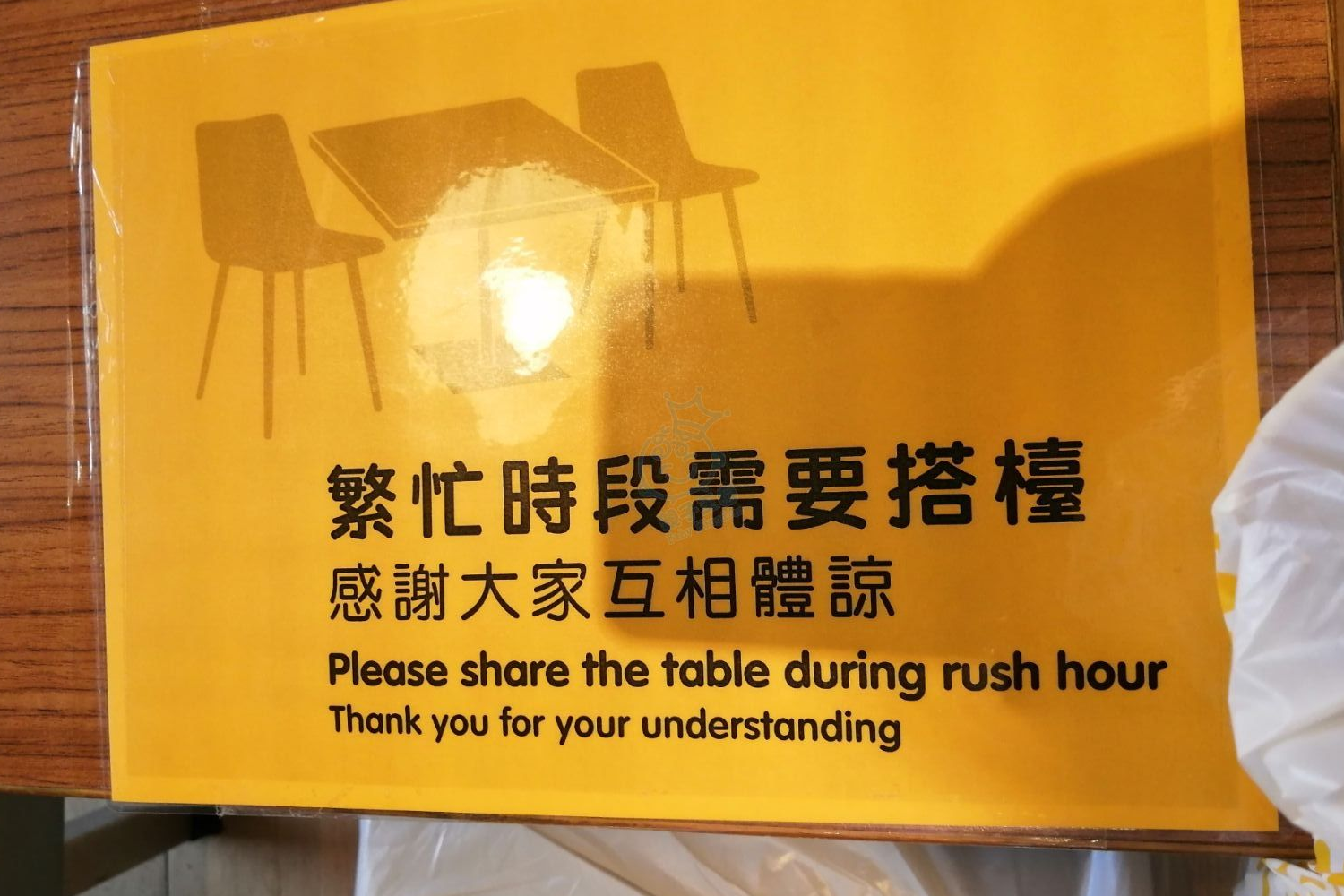 餐廳內要求客人在繁忙時段共享餐桌的告示牌，這是一種在香港常見的餐桌文化習慣。