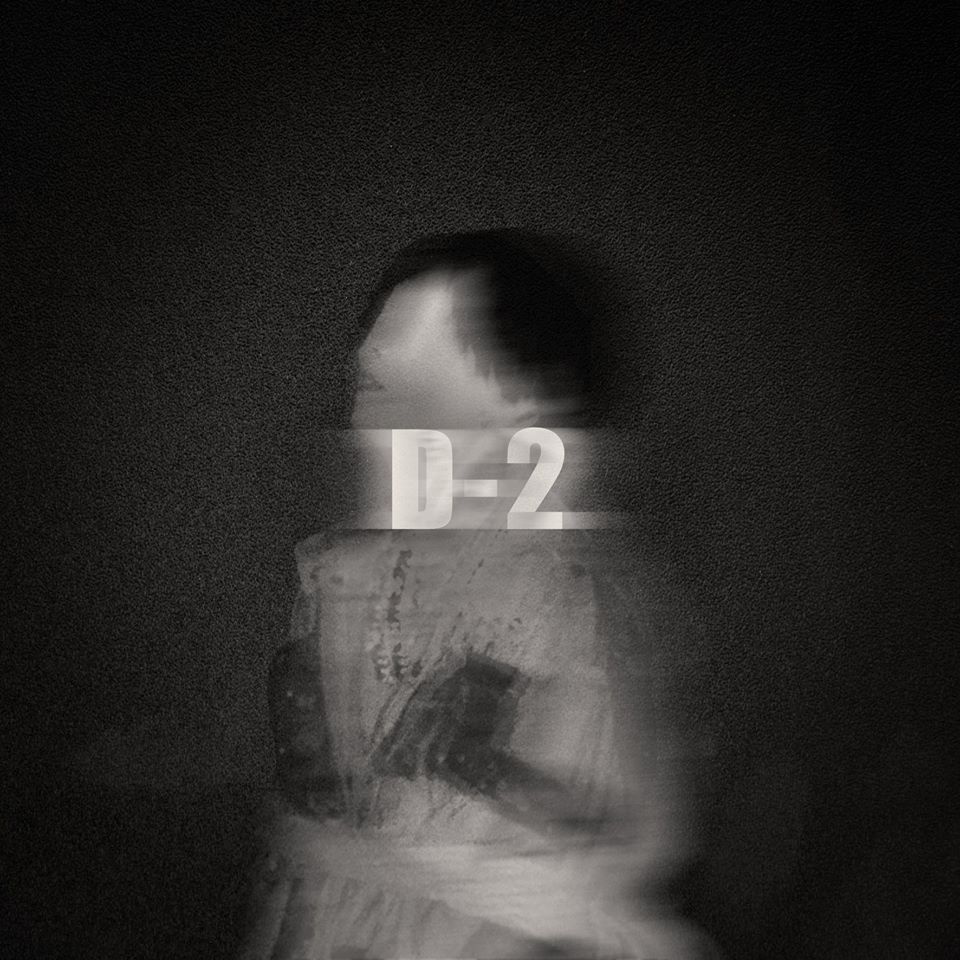 Чёрно-белое изображение с текстом 'D-2' на переднем плане, предполагаемая тизерная фотография Agust D.