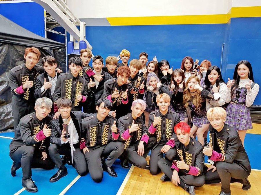 กลุ่มศิลปินที่ประกอบด้วยทั้งชายและหญิงในชุดสีดำที่มีลวดลายทอง ยืนรวมตัวกันในห้องยิมพร้อมชูนิ้วโป้ง ร่วมฉลองความสำเร็จร่วมกัน