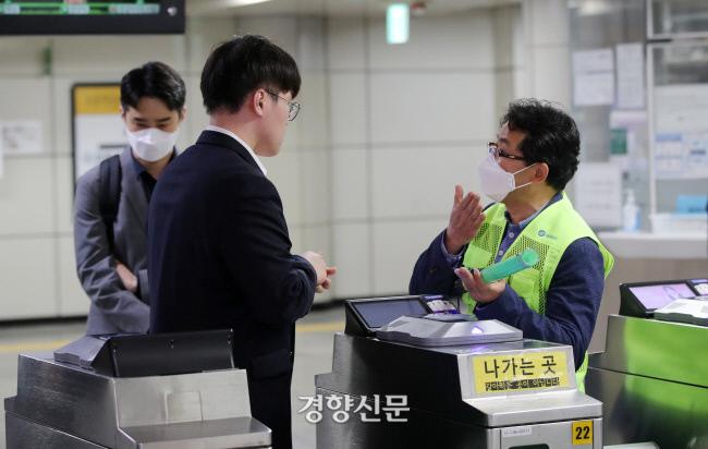 地鐵站內工作人員與乘客交流場景，工作人員穿著綠色背心，疫情期間安全措施的實施。