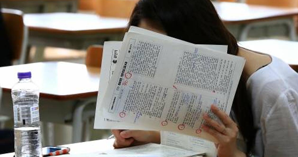 Một sinh viên ngồi trên sân trường Hàn Quốc, cầm tập sách che mặt. Tâm trạng lo lắng. Phong trào truyền thống giáo dục nghiêm ngặt của Hàn Quốc đối với sinh viên mới.