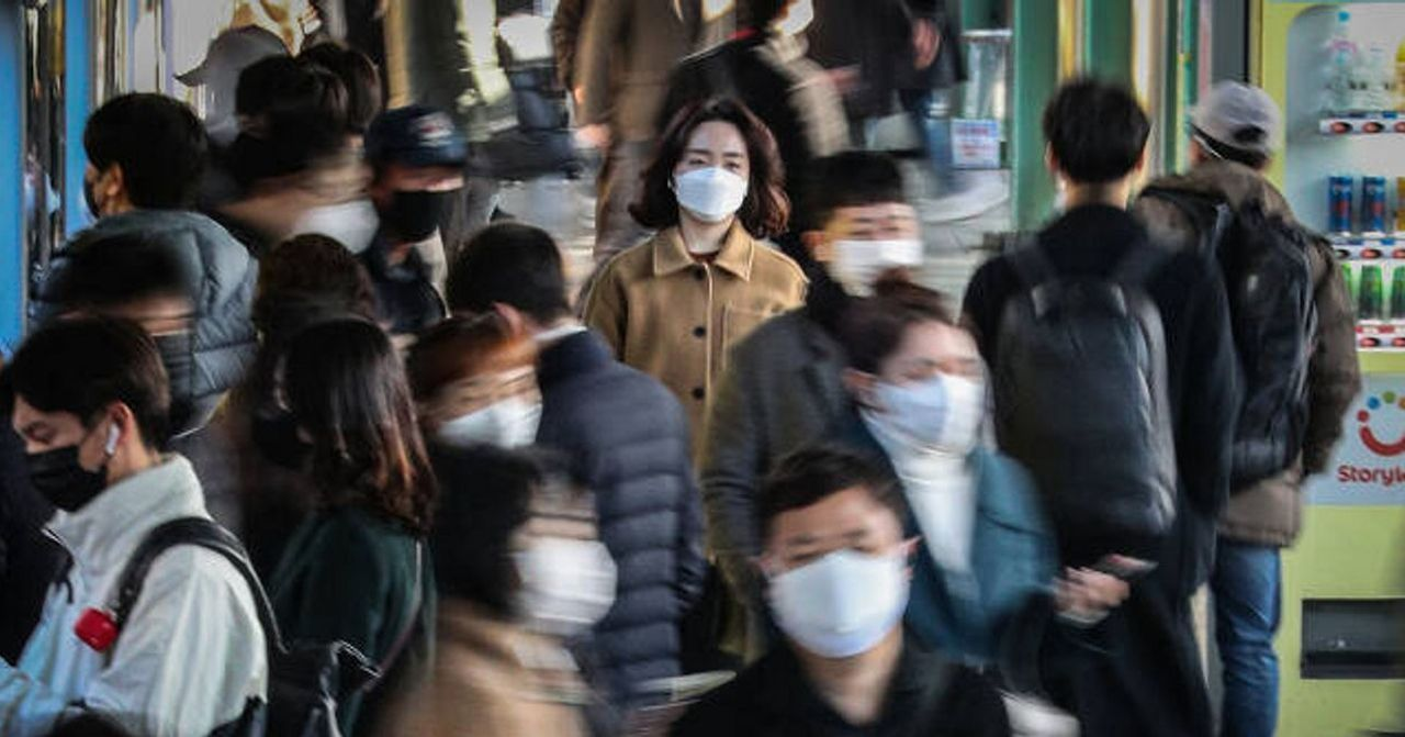 香港地鐵乘客在通勤時間配戴口罩的場景，乘客們穿著秋冬服飾，地鐵站內擠滿人潮，上班族與學生們聚集在一起。