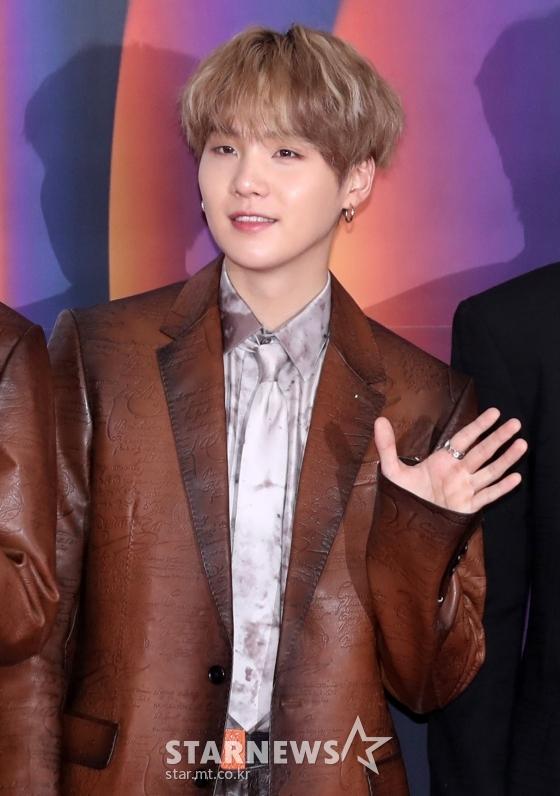 防弾少年団BTSのメンバーSUGAが茶色のジャケットを着て手を振っている
