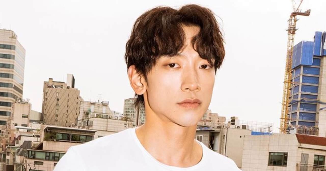 韓國著名藝人Rain於陽光明媚的城市背景中穿著白色上衣面帶微笑