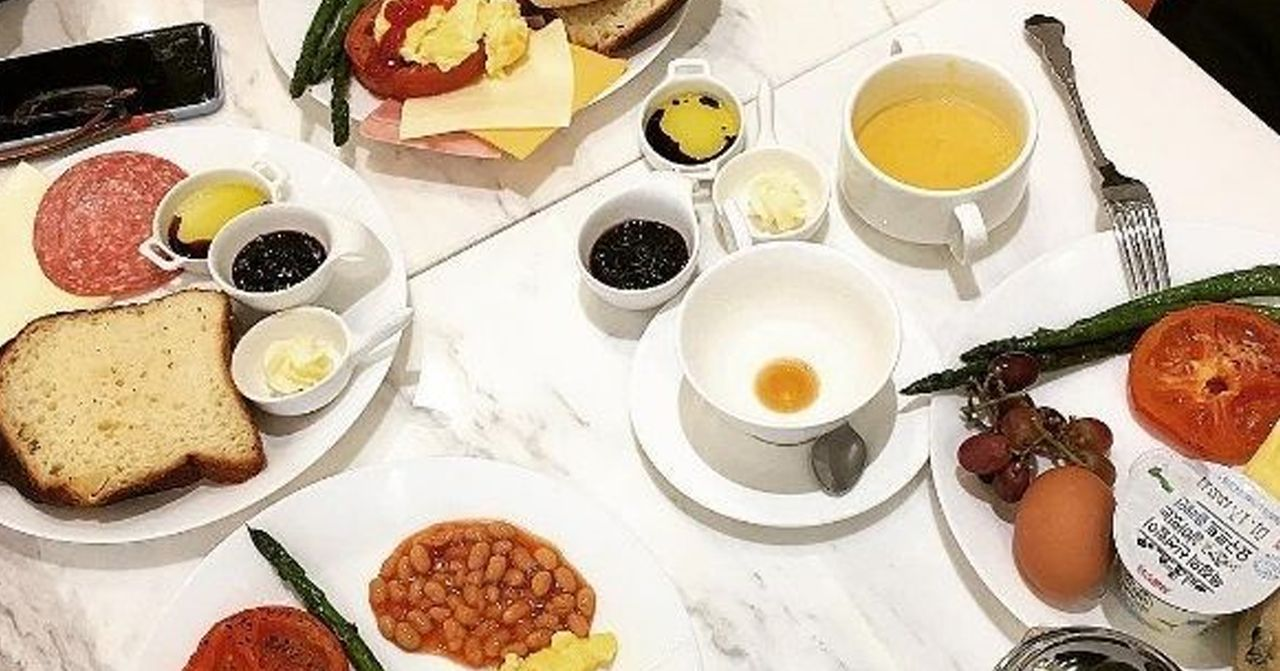 อาหารถ่ายจากมุมบนที่มีอาหารเช้าครบหลากหลาย ประกอบด้วยถั่วอบ ไข่ไก่ ผัก สลัด และขนมปัง บนโต๊ะหินอ่อนสีขาว พบได้ในร้านอาหารหรือโรงแรมในโซล