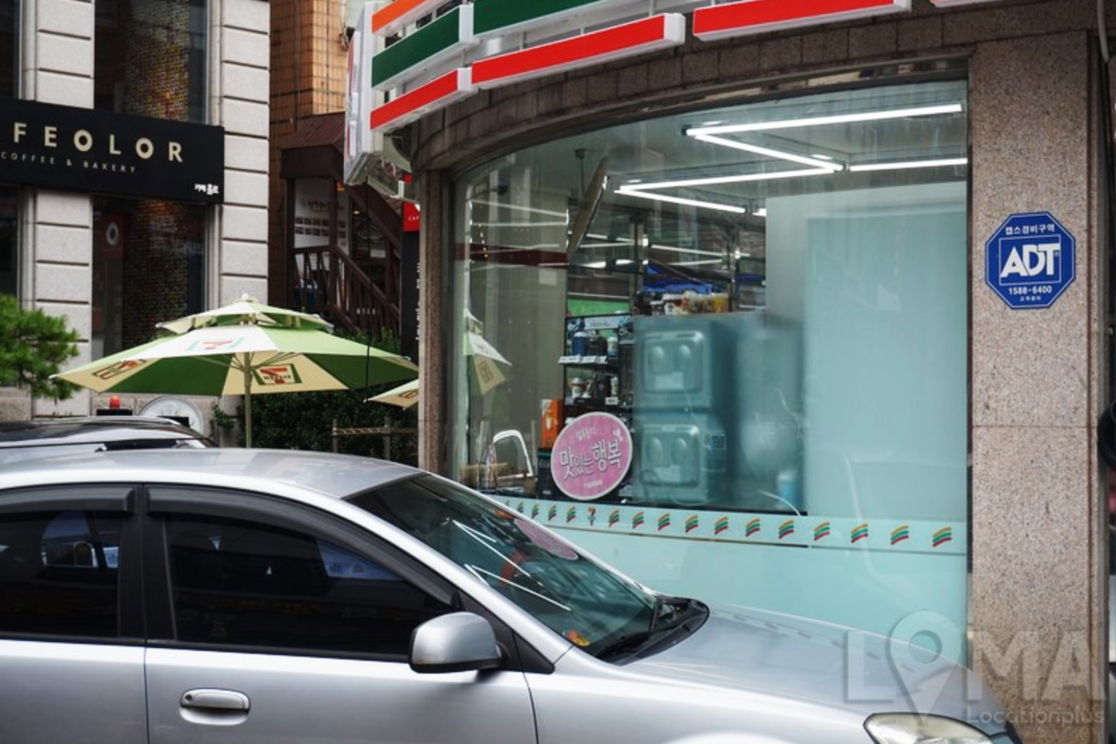 Vista externa de una tienda Seven Eleven ubicada en una intersección de calles concurridas. Se observa la señal de ADT en la esquina del edificio.