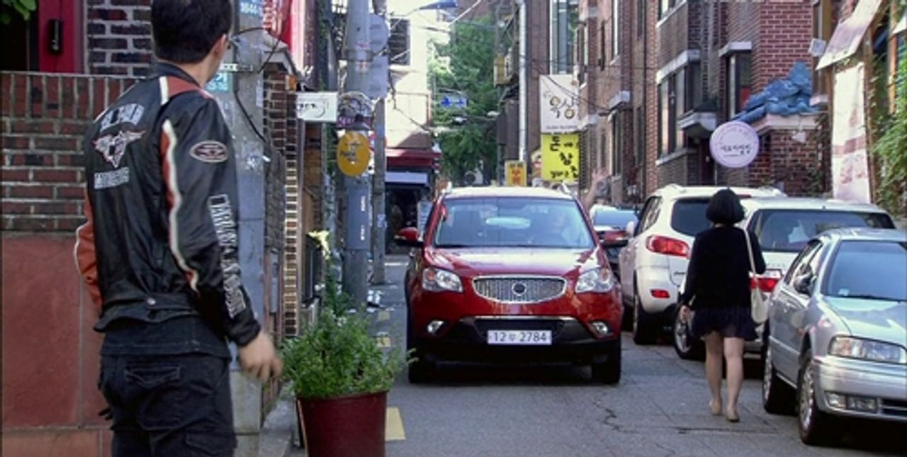 韓國街道旁停著一輛紅色的汽車，背景是韓國的都市小巷。