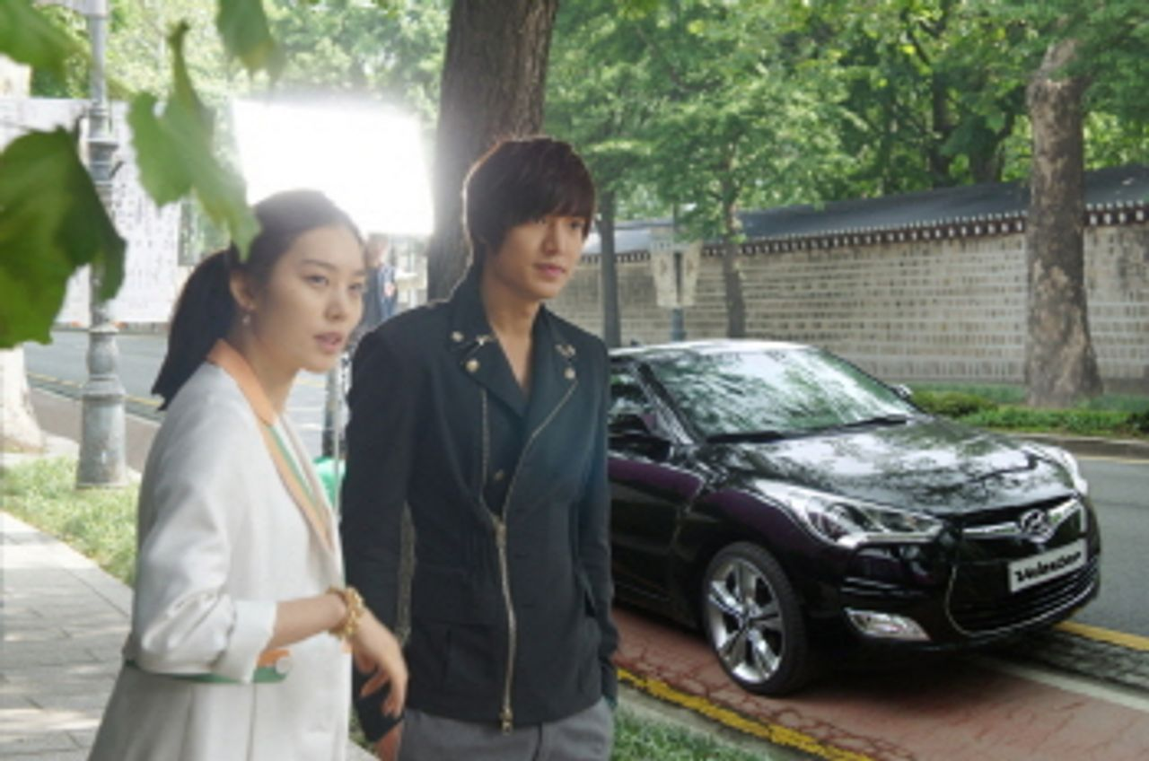 街道上停著一輛黑色的汽車，背景是樹木和建築物。