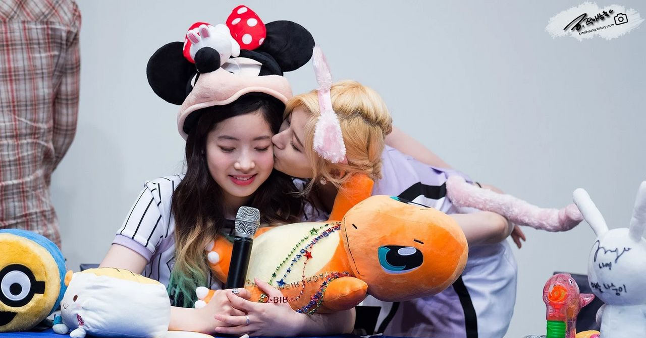 身穿米奇帽子的女孩被朋友從後擁抱，一起坐在桌前。