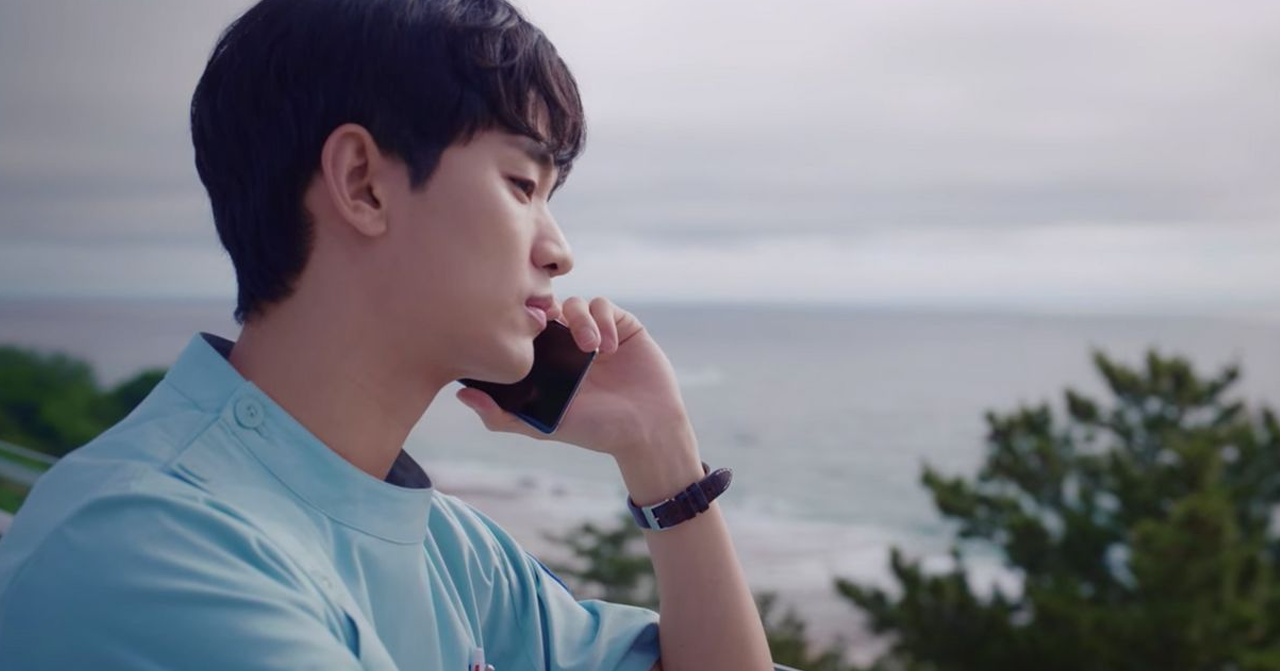 穿著藍色襯衫的角色在室外打電話，背景是海景。