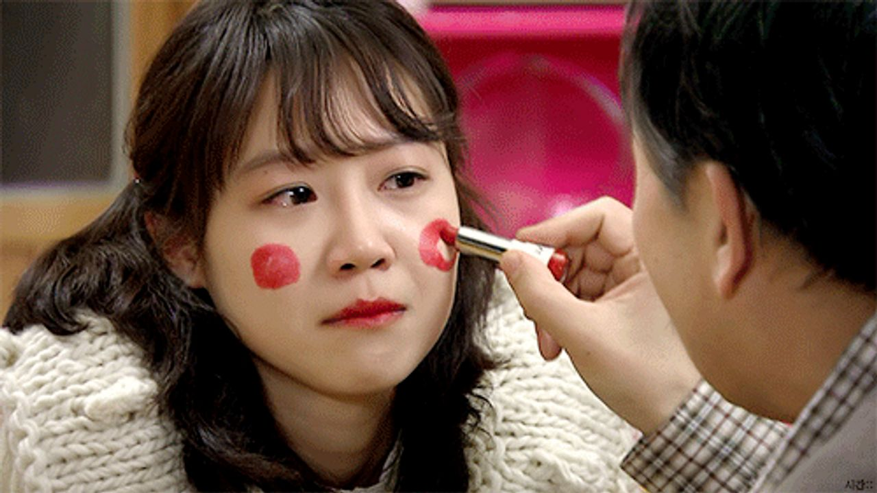 角色在韓國室內場景中被人用小道具碰觸臉部。